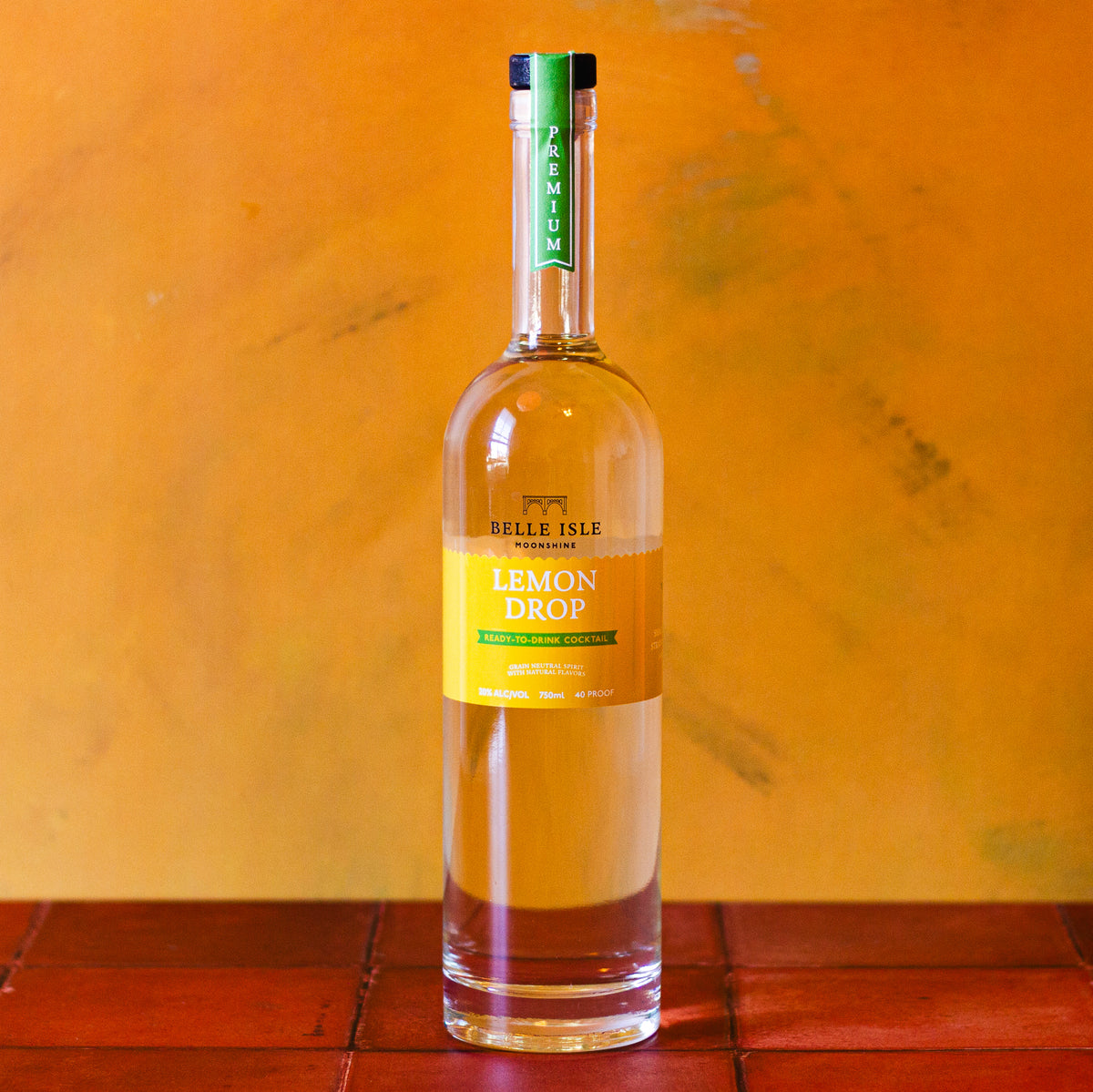 A bottle of Belle Isle Lemon Drop moonshine with a clear liquid visible through the transparent bottle. The label is yellow with green text and accents.