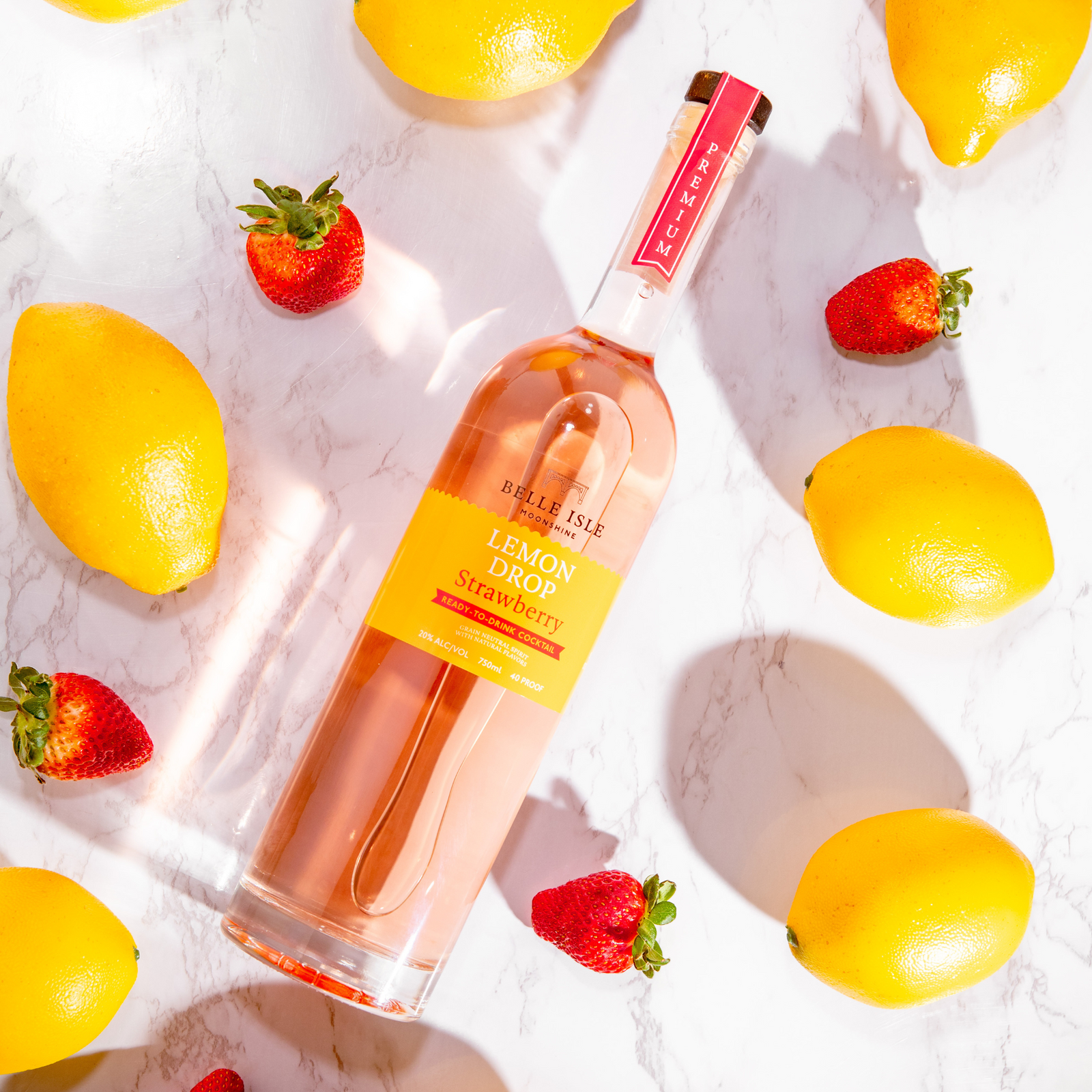 A bottle of Belle Isle Lemon Drop Strawberry moonshine 750ml surrounded by lemons and strawberries on a marble surface.