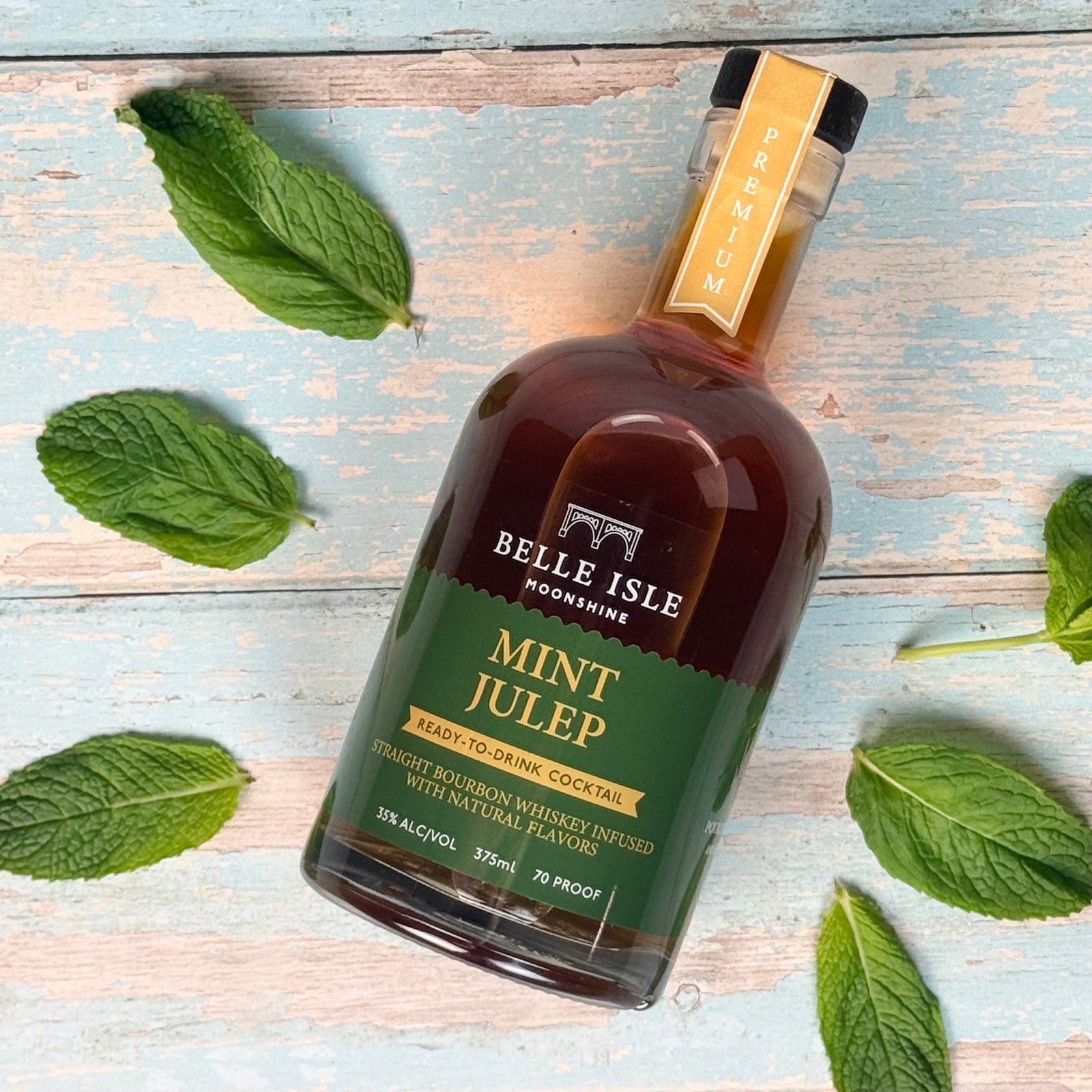 A bottle of Belle Isle Mint Julep bourbon whiskey on a wooden surface surrounded by fresh mint leaves.